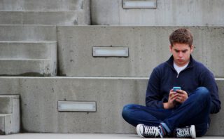 Teenager Junge sitzt auf Betonstufen Handy