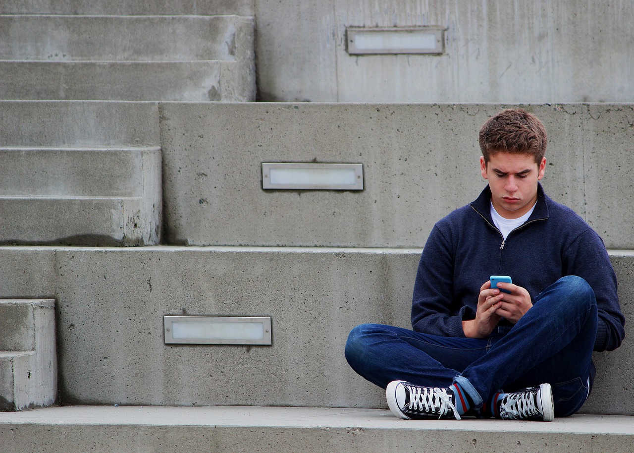 Teenager Junge sitzt auf Betonstufen Handy